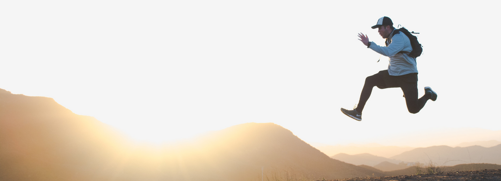 Guy Jumping rocks with a backpack on and trucker hat